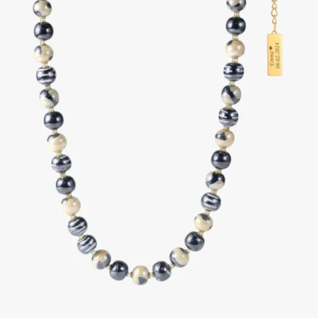 Denne elegante halskæde fra Kazuri er et sandt kunstværk i keramik. Halskæden består af håndlavede og håndmalede perler i smukke nuancer af sort, rosa og grå, kombineret med dekorative mønstre, der giver smykket et levende og unikt udtryk. Hver perle er fremstillet med stor omhu af kvindelige kunsthåndværkere i Kenya. Da alle perler er håndlavede, er ingen halskæder ens – hvilket gør dit smykke helt personligt og unikt. Kazuri arbejder efter Fair Trade-principper, så du får et smykke med både sjæl og en stærk historie om bæredygtighed og kvinders empowerment.